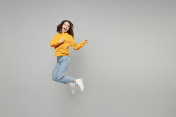 Full length of young excited overjoyed expressive woman in knitted yellow sweater run fast in air jump high point index finger aside on workspace mock up isolated on grey background studio portrait..