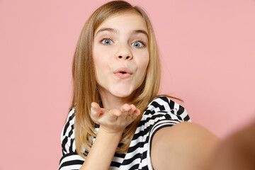 Wall Mural - Close up little blonde romantic lovely kid girl 12-13 year old in striped oversized t-shirt do selfie shot on mobile phone show blowing air kiss isolated on pink background children Childhood concept