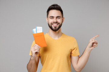 Wall Mural - Traveler young tourist man in yellow t-shirt hold passport tickets point finger aside on workspace isolated on grey background Passenger travel abroad weekends getaway Air flight journey concept