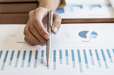 Close-up businesswoman's hand holding a pen pointing at a bar chart on a corporate financial information sheet, the businesswoman examines the financial information provided by the finance department.