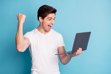 Poster - Portrait of astonished man arm hold laptop fist up open mouth scream yeah isolated on blue color background