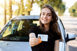 Pretty girl with cheerful smile standing near the car and showing driving license to the camera. Woman expresses her happiness after passing the driving exam.