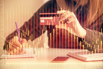 Double exposure of woman on-line shopping holding a credit card and financial graph drawing. Stock market E-commerce concept.