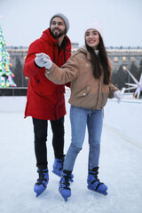 Wall Mural - Happy young couple skating at outdoor ice rink