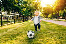 Happy Little Kid Playing Soccer Ball In The Park. Children Are Playing Football