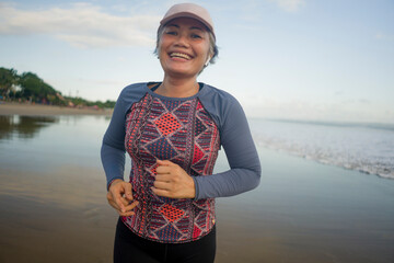 fit and attractive mature woman with grey hair doing beach workout on her 50s running on the beach happy and free in senior fitness selfcare and wellness concept