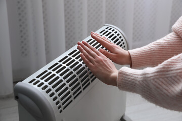 Wall Mural - Woman warming hands near electric heater at home, closeup