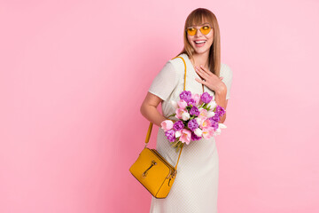 Poster - Portrait of attractive impressed cheerful girl holding in hands flowers looking aside copy space isolated over pink pastel color background