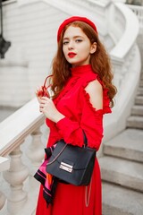 Wall Mural - Outdoor portrait of fabulous ginger girl in red beret and dress standing on stairs near bridge in Paris. Luxury purse. Gorgeous healthy hairs.