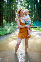 Wall Mural - Young mother holding her son and standing in the puddle in the forest