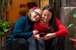 Candid portrait of two female friends chatting, laughing and using a smart phone