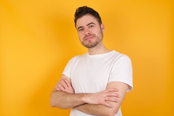 Wall Mural - Waist up shot of  self confident young handsome Caucasian man against yellow wall has broad smile, crosses arms, happy to meet with colleagues.