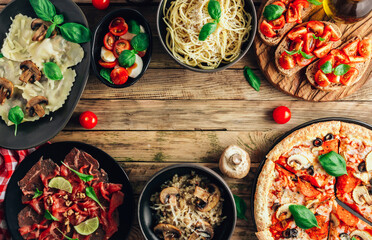 Wall Mural - Table of italian meals on plates Pizza, pasta, ravioli, carpaccio, mushroom risotto, caprese salad and tomato bruschetta on rustic wooden background.