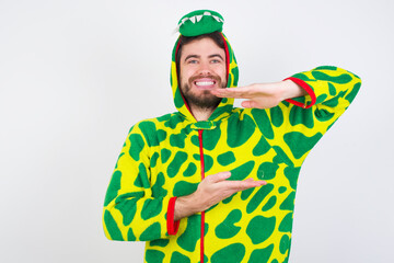 Sticker - young caucasian man wearing a pyjama standing against white wall gesturing with hands showing big and large size sign, measure symbol. Smiling looking at the camera.