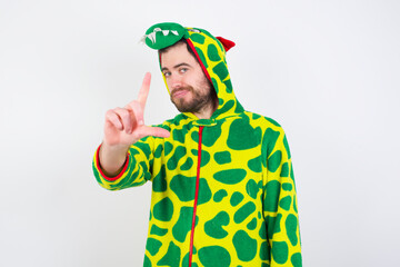 Sticker - young caucasian man wearing a pajama standing against white background making fun of people with fingers on forehead doing loser gesture mocking and insulting.