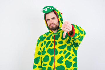 Sticker - young caucasian man wearing a pajama standing against white background feeling angry, annoyed, disappointed or displeased, showing thumbs down with a serious look