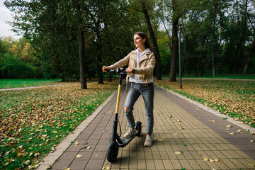 Young beautiful stylish woman riding electric scooter by autumn park, ecological transport