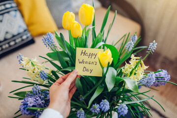 Wall Mural - Happy Womens Day, 8 March gift. Woman holds greeting card with blooming spring yellow blue flowers at home