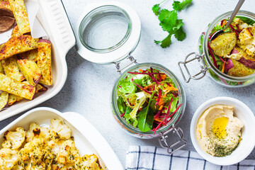 Wall Mural - Cooking healthy food concept. Baked cauliflower, sweet potato, hummus and salad in jars on gray background, top view. Cooking food for the week.