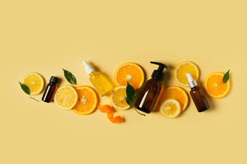 Bottles of serum of vitamin c and orange, lemon and green leaf flat lay on yellow background