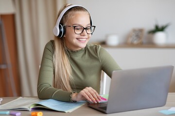 Cute school girl having online lesson, using laptop at home