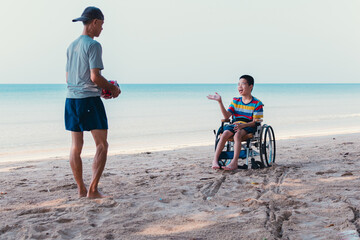 Asian special child on wheelchair is fun, playing ball and exercise activity on sea beach at summer, Lifestyle of disability child, Life in the education age, Happy disabled kid in travel concept.