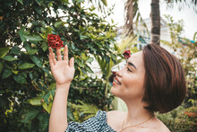 A Pretty Short Haired Asian Lady Wearing An Off Shoulder Top Admires A Hibiscus Flower Bud That Has Not Bloomed Yet At A Garden.