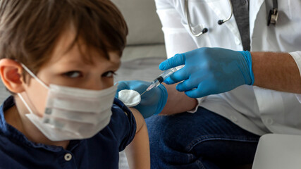 Wall Mural - Doctor holding a vaccine syringe. Little boy is ready to get a shot. Pediatrician makes vaccination to small boy at home. Doctor vaccinating child. Little boy getting flu shot. Coronavirus vaccination