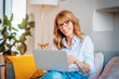 © sepy - Happy mature woman using laptop while sitting on the couch at home