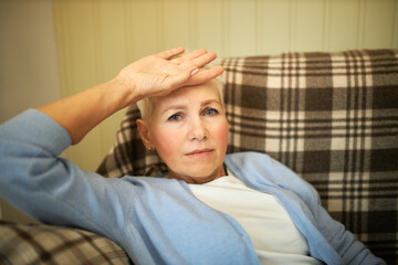 Indoor shot of unhappy mature Caucasian woman looking at camera with worried frustrated facial expression holding hand on her head waiting for doctor while lying on sofa, feeling sick, having fever