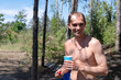 © domarevatanya - Young adult bare-chested man enjoys a vacation in nature on a hot summer day. He smiles holding a glass and cherry in the background of the trees