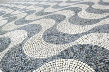 Photo Of Paving Stones In Perspective. The Drawing Is Lined With Cobblestones In The Form Of White And Gray Waves. Traditional Street Paving In Lisbon And Rio De Janeiro.
