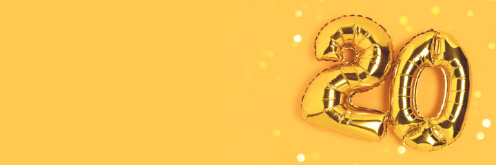 Banner with number 20 golden balloons with copy space. Twenty years anniversary celebration concept on a yellow background with shiny bokeh.