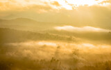 Fototapeta Na drzwi - mountain covered with white mist and orange sun rays at dawn