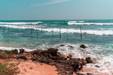 Fototapeta Fototapety z morzem do Twojej sypialni - Tropikalna plaża z palmami, niebieski ocean z falami oraz kije rybackie.