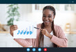 © Prostock-studio - Smiling Black Financial Analyst Woman Making Teleconference From Home, Showing Financial Report