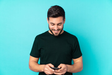 Poster - Caucasian handsome man isolated on blue background sending a message with the mobile