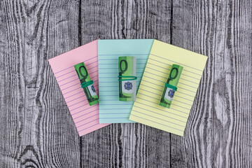 Fototapete - Rolls of 100 Euro banknotes on colored notepads arranged fanned to the centre of the screen on a wood background in an overhead view for financial concepts. Flat lay, top view