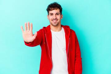 Wall Mural - Young caucasian man isolated on blue background smiling cheerful showing number five with fingers.