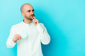 Young caucasian bald man celebrating world water day isolated on blue background looking sideways with doubtful and skeptical expression.