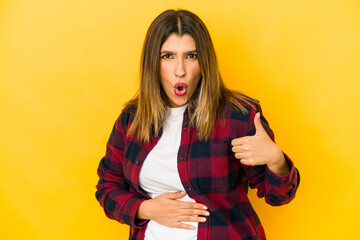 Young indian woman isolated on yellow background touches tummy, smiles gently, eating and satisfaction concept.