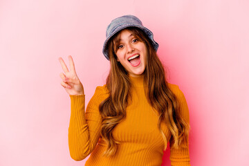 Wall Mural - Young caucasian woman wearing fishermans hat isolated joyful and carefree showing a peace symbol with fingers.