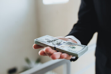 One hundred dollar bills money bundle, in hand of man in suit and white shirt