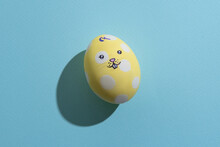 Happy Easter. Funny Bunny Decor. Festive Gift. Holiday Celebration. Colorful Egg Of Yellow White Spotted Pattern And Painted Pretty Snout Isolated On Blue Textured Copy Space.