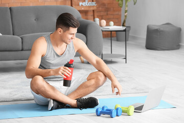 Wall Mural - Sporty young man with laptop training at home