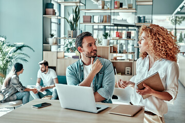 Wall Mural - Confident businessman and businesswoman discussing business plan in cafe