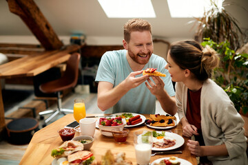 Happy couple having fun while eating waffles for breakfast at dining table.