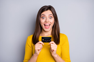 Wall Mural - Portrait of attractive amazed cheerful girl holding in hands bank card having fun funds isolated over grey color background