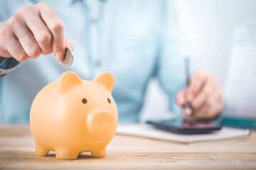 Close up businessman hand putting money coin into piggy for saving money, budget, investment or strategy for personal savings