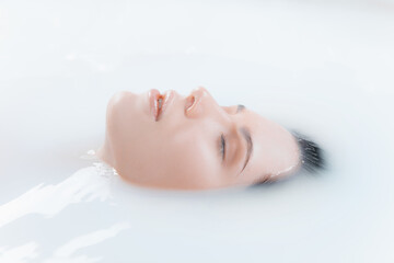 Close up female face in the milk bath with soft white glowing. Copyspace for advertising. Beauty, fashion, style, bodycare concept. Attractive caucasian model in milky colored foam.